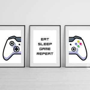 Könnte beinhalten: Drei gerahmte Drucke mit weißem Hintergrund. Der mittlere Druck zeigt den Text "Eat Sleep Game Repeat" in Schwarz. Die linken und rechten Drucke zeigen jeweils einen weißen Videospiel-Controller mit schwarzen Knöpfen und einer grauen Umrandung.