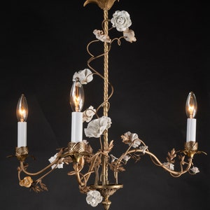 May include: A gold chandelier with white porcelain flowers and three candle-style light bulbs.