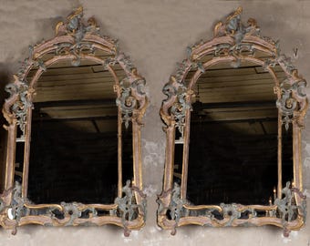 May include: A pair of arched wall mirrors featuring ornate, carved frames with a distressed finish. The frames combine metallic gold accents with muted, weathered blue-green tones, showcasing intricate scrollwork and decorative floral motifs.