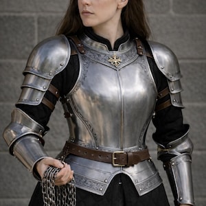May include: A polished steel breastplate and arm armor with decorative etching and a brown leather belt. The armor is worn over a black garment. A chain is held in the hand.