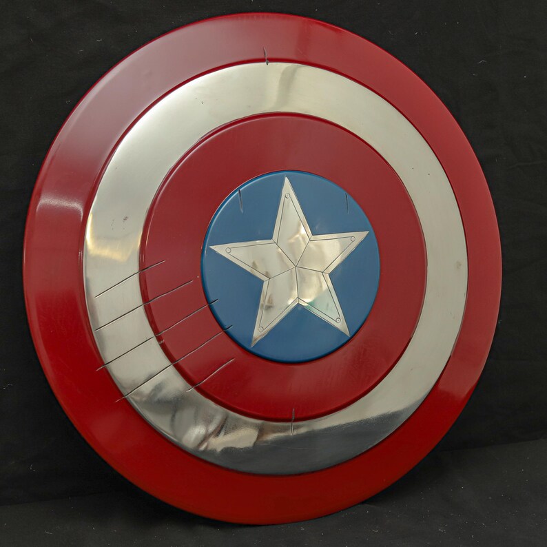 May include: A round shield with a red outer ring, a silver middle ring, and a blue center with a silver star. The shield has a glossy finish and appears to be made of metal. The shield has several scratches on the silver ring.