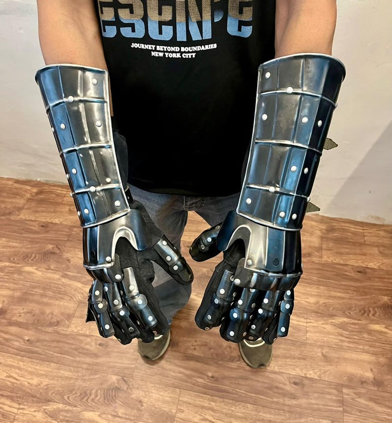 May include: Black metal gauntlets with articulated fingers and wrist protection. The gauntlets are riveted and have a polished finish. The design includes a series of plates and studs, offering a medieval aesthetic. The gauntlets are shown against a neutral background.