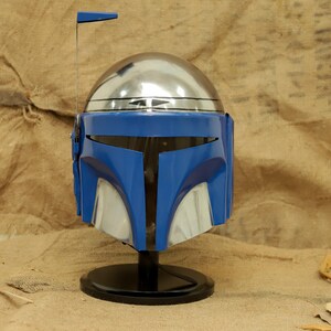 May include: A blue and silver helmet with a black base. The helmet has a shiny silver dome and a blue faceplate with silver accents. A small antenna extends from the top. The helmet is a prop or collectible.