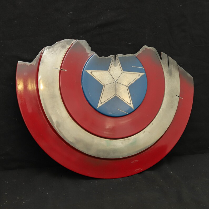 May include: A red, white and blue Captain America shield with a star in the centre. The shield is damaged and has a chipped edge.