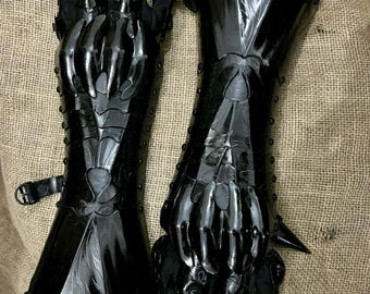 Puede incluir: Par de guanteletes negros articulados con extensiones afiladas en forma de garra. Los guanteletes presentan detalles intrincados y están hechos de un material oscuro y brillante. El diseño sugiere un tema de fantasía o cosplay.