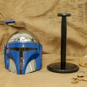 May include: A blue and silver helmet with a black stand. The helmet has a silver dome and blue faceplate with silver accents. The black stand has a round base and a vertical pole.