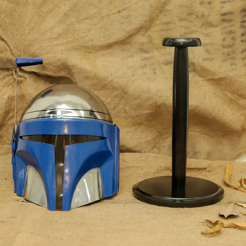 May include: A blue and silver helmet with a black stand. The helmet has a silver dome and blue faceplate with silver accents. The black stand has a round base and a vertical pole.