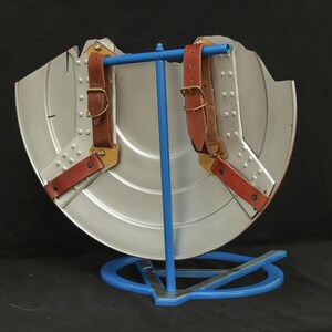 May include: The back of a silver Captain America shield with brown leather straps and gold buckles. The shield is on a blue metal stand.