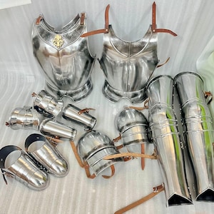 May include: A collection of polished steel armor pieces, including breastplates, helmets, arm and leg guards, and gauntlets. The armor features decorative detailing and leather straps. The breastplates have a gold emblem.