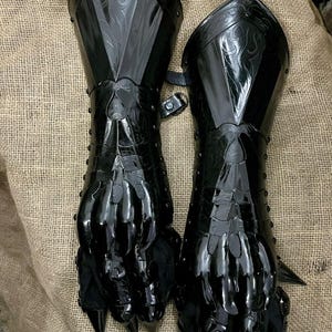 May include: Pair of black, articulated gauntlets with a claw-like design. The armor features decorative etching on the upper arm and is secured with a buckle. The gauntlets have sharp, pointed claws at the fingertips.