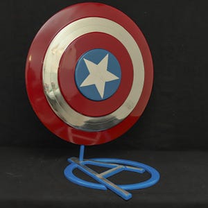 May include: A red, white, and blue Captain America shield with a silver rim, displayed on a blue stand with a silver Avengers logo.