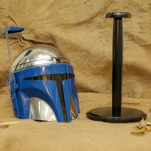 May include: A blue and silver helmet with a black visor and a matching black stand. The helmet has a unique design with a silver dome and blue faceplate. The stand is black and round.