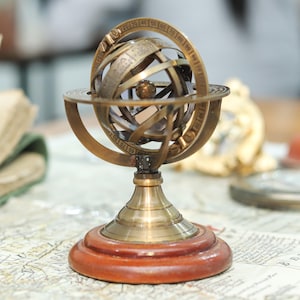 May include: A brass celestial globe on a wooden base. The globe is a sphere with a grid of lines and numbers, representing the Earth's latitude and longitude. The globe is mounted on a stand with a circular base.