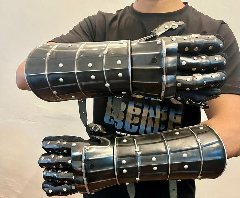 May include: Pair of black metal gauntlets with riveted accents. The gauntlets are segmented, with articulated fingers and wrist protection. They are designed to cover the entire hand and forearm, with leather straps for securing them.
