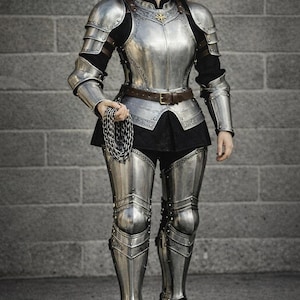 May include: Full suit of polished steel armor, including a breastplate, pauldrons, arm and leg protection, and boots. The armor is worn over a black outfit, with a brown belt. A chain is held in the hand.