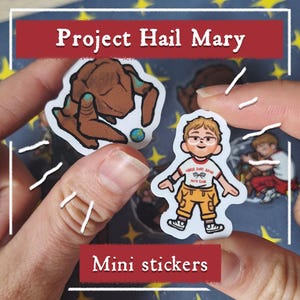 May include: Mini stickers featuring characters from "Project Hail Mary." One sticker depicts a brown, alien-like figure with a blue orb. Another shows a cartoon of a person in a white shirt with the text "Horse Shoe Bend Auto Club" and yellow pants.