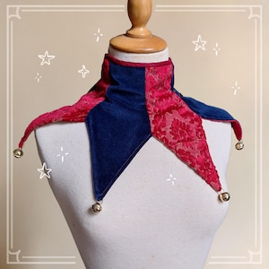 K&ouml;nnte beinhalten: Ein Narrenkragen in Rot und Marineblau mit goldenen Gl&ouml;ckchen. Der Kragen hat einen hohen Kragen und ein Rautenmuster, mit einer Samtstruktur und einem dekorativen floralen Spitzendesign auf den roten Abschnitten.