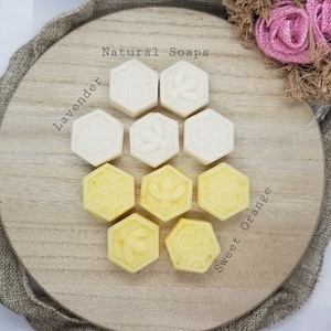May include: Natural soaps in a honeycomb design. The soaps are arranged in a circle on a wooden tray. The soaps are labeled "Lavender" and "Sweet Orange".