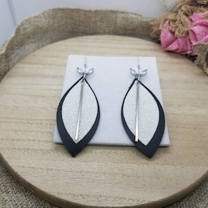 May include: A pair of dangle earrings with a white glitter leaf design and black leather trim. The earrings have a silver metal bar and a clear crystal at the top.