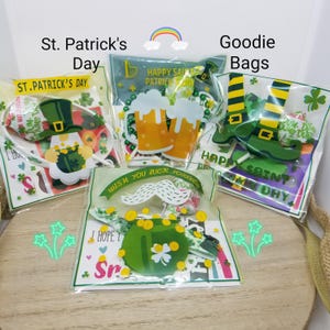 May include: Four clear plastic bags filled with St. Patrick's Day themed goodie bag items. The bags contain a variety of green, gold, and white decorations, including a leprechaun, a pot of gold, a beer mug, and a pair of green boots. The bags are labeled "St. Patrick's Day" and "Goodie Bags".