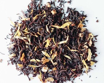 May include: A close-up of a blend of black tea leaves and dried mango pieces. The tea leaves are dark brown and the mango pieces are a bright yellow.