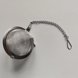 May include: A silver tea infuser with a fine mesh ball and a chain with a hook.