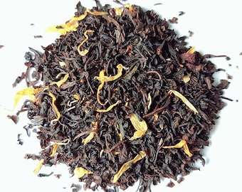 May include: A close-up of a pile of black tea leaves with orange peel pieces. The tea leaves are loose and have a dark brown color. The orange peel pieces are bright orange and add a citrusy flavor to the tea.