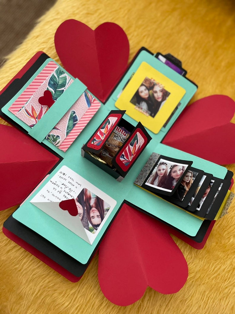 Pu&ograve; includere: Una scatola esplosiva turchese e rossa con un coperchio a forma di cuore. La scatola &egrave; decorata con foto, carta fantasia e una piccola scatola regalo. Il testo all'interno della scatola dice "Buon compleanno!" e "Spero che tu abbia una giornata meravigliosa!"