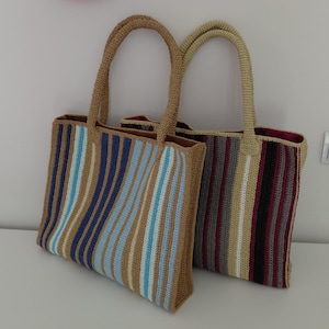 May include: Two rectangular crochet tote bags with vertical stripes. The front bag features tan, blue, and white stripes. The back bag features maroon, grey, tan, and white stripes. Both bags have matching crochet handles and a solid interior lining.