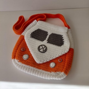 May include: A crochet crossbody bag featuring an orange and white color scheme designed to resemble a vintage van. The bag includes a white front panel with dark gray windshield details, a circular gray emblem, and small gray circular headlights.