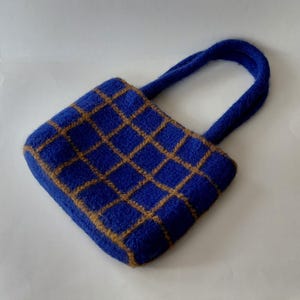 Könnte beinhalten: Kleine, quadratische Handtasche in Blau mit einem beigefarbenen Gittermuster. Sie hat einen passenden blauen Griff. Die Tasche ist aus einem weichen, strukturierten Material gefertigt.