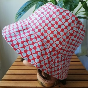 Peut inclure: Un chapeau de seau à motifs rouges et bleu clair. Le chapeau présente un motif floral répétitif en bleu clair sur un fond rouge. Le chapeau en tissu est doté d'un bord pour la protection solaire. Le chapeau est présenté sur une tête de mannequin.