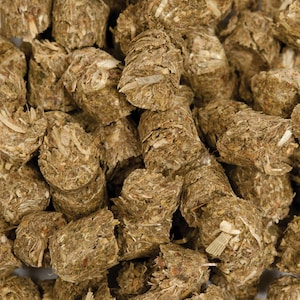 May include: Close-up of a pile of compressed, cylindrical animal feed pellets. The pellets are a mix of brown and green hues, with visible fibrous material. The texture appears rough and natural, suggesting a hay-based composition. The image is well-lit, highlighting the details.