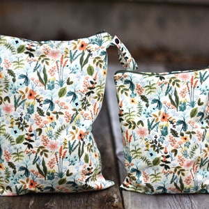 May include: Two zippered bags with a floral print. The larger bag is white with green, orange, and pink flowers. The smaller bag is the same print but smaller. Both bags have a zipper closure and a loop handle.