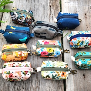 May include: Ten small zippered pouches with various floral and geometric patterns. The pouches are made of fabric and have a zipper closure. They are all different colors and patterns, including blue, green, pink, orange, and white.