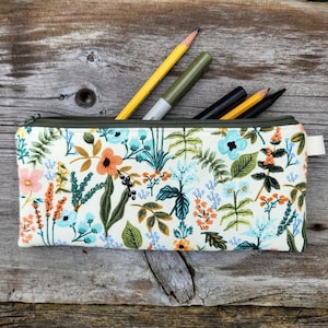 May include: A floral print pencil case with a green zipper, containing a yellow pencil, a green marker, and two other pencils. The case features a cream background with orange, blue, and pink flowers and green leaves.