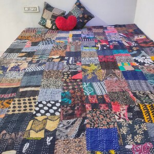 May include: A patchwork quilt made from a variety of fabrics in shades of blue, brown, black and white. The quilt is made up of squares of different fabrics sewn together. The quilt is on a bed with two pillows and a heart-shaped pillow.