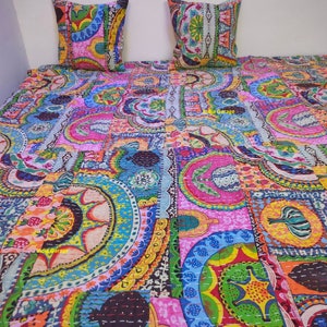 Könnte beinhalten: Eine farbenfrohe Kantha-Steppdecke mit Patchwork-Design, das verschiedene geometrische Formen und Blumenmuster zeigt. Die Steppdecke ist aus recycelten Saris gefertigt und handgenäht. Die Steppdecke wird mit zwei passenden Kissenbezügen gezeigt.