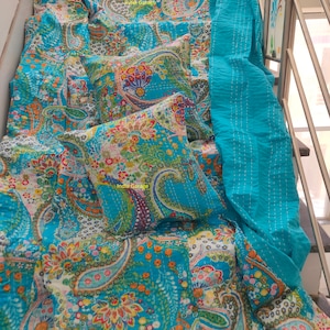 Może przedstawiać: Turkusowa kołdra kantha z wzorem paisley w odcieniach pomarańczowego, żółtego, zielonego i różowego. Kołdra jest złożona na schodach i ma pasującą poduszkę z nadrukiem "India Garage".