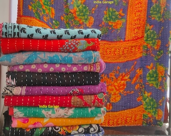 May include: A stack of colorful kantha quilts with floral patterns. The quilts are folded and stacked on top of each other. The top quilt is a purple and orange floral pattern with a gold border. The text "India Garage" is visible on the top quilt.