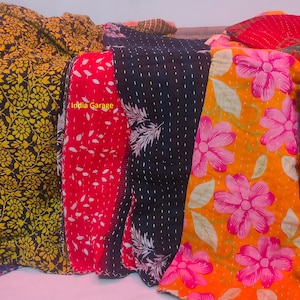 Peut inclure: Une collection de six quilts kantha color&eacute;s avec des motifs floraux et g&eacute;om&eacute;triques. Les quilts sont faits de saris recycl&eacute;s et sont cousus &agrave; la main. Les quilts sont dispos&eacute;s en rang&eacute;e, avec le texte "India Garage" visible sur l'un des quilts.