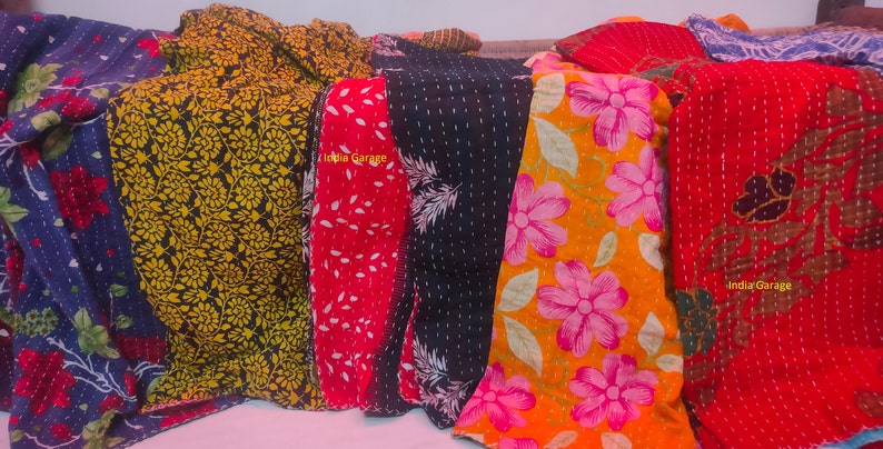 Peut inclure: Une collection de six quilts kantha color&eacute;s avec des motifs floraux et g&eacute;om&eacute;triques. Les quilts sont faits de saris recycl&eacute;s et sont cousus &agrave; la main. Les quilts sont dispos&eacute;s en rang&eacute;e, avec le texte "India Garage" visible sur l'un des quilts.