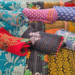 Peut inclure: Une collection de courtepointes kantha color&eacute;es, cousues &agrave; la main &agrave; partir de saris recycl&eacute;s, pr&eacute;sentant des motifs floraux et g&eacute;om&eacute;triques. Les courtepointes sont roul&eacute;es et dispos&eacute;es sur un escalier, mettant en valeur leurs d&eacute;tails complexes et leurs teintes vibrantes.