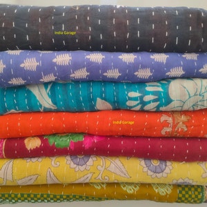 Peut inclure: Une pile de huit quilts kantha color&eacute;s avec diff&eacute;rents motifs floraux et g&eacute;om&eacute;triques. Les quilts sont faits de saris recycl&eacute;s et sont cousus &agrave; la main. Le texte "India Garage" appara&icirc;t sur deux des quilts.