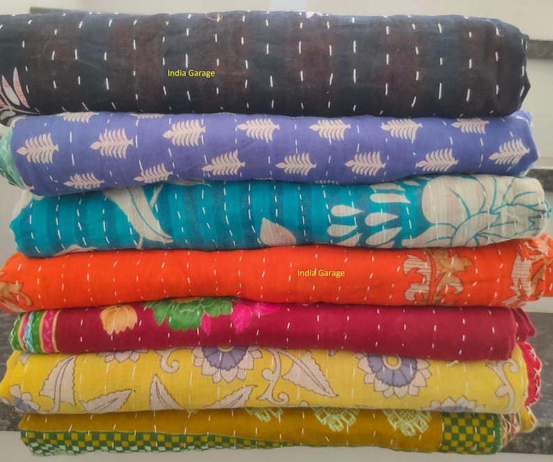 Peut inclure: Une pile de huit quilts kantha color&eacute;s avec diff&eacute;rents motifs floraux et g&eacute;om&eacute;triques. Les quilts sont faits de saris recycl&eacute;s et sont cousus &agrave; la main. Le texte "India Garage" appara&icirc;t sur deux des quilts.