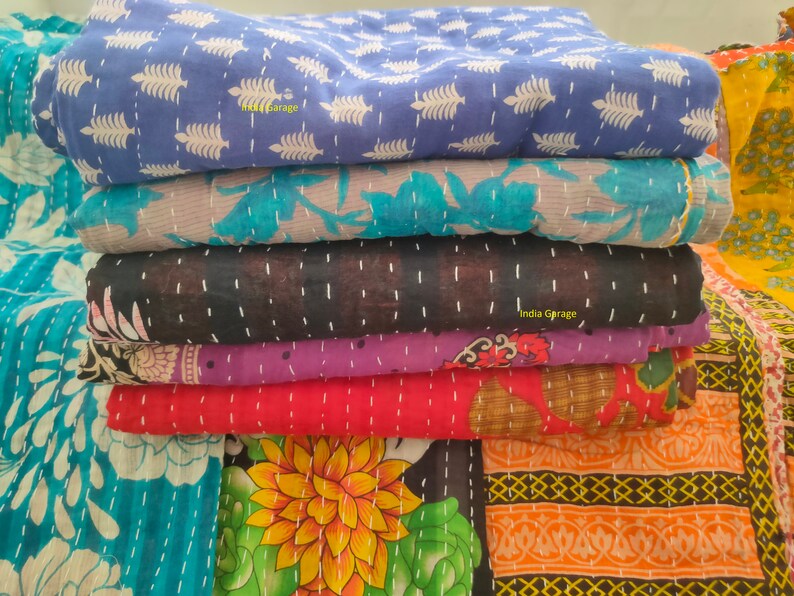 Peut inclure: Une pile de six quilts kantha de diff&eacute;rentes couleurs et motifs, notamment bleu, turquoise, noir, violet, rouge et orange. Les quilts sont en coton et pr&eacute;sentent un motif cousu &agrave; la main. Le texte "India Garage" est visible sur le quilt du bas.