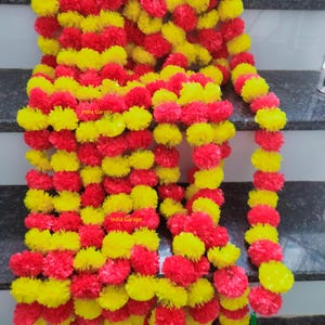 Op de afbeelding: Een levendige slinger bestaande uit afwisselende secties van gele en rode pom-pom-achtige bloemen. De slinger is dicht opeengepakt, waardoor een volle en getextureerde uitstraling ontstaat. De tekst "India Garage" is zichtbaar.