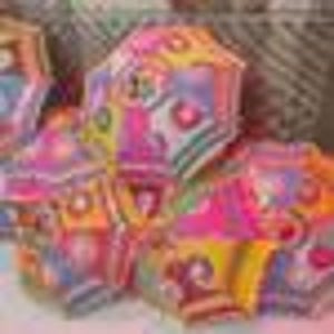 Puede incluir: Una colección de faroles de papel geométricos y coloridos. Cada farol presenta un patrón único con tonos de rosa, amarillo, azul y naranja. Los faroles tienen forma hexagonal y parecen estar hechos de papel plegado.