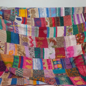 May include: A colourful patchwork quilt made from recycled saris. The quilt is made up of many different colours and patterns, including floral, geometric, and paisley designs. The quilt is hand-stitched and has a unique, vintage look.