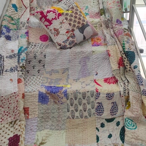 以下が含まれることがあります： パッチワークのキルトと、それに合うクッション2つ。キルトとクッションは、花柄、幾何学模様、抽象的なデザインなど、さまざまな生地のパターンと色を使用しています。キルトは表面に掛けられ、クッションが上に配置されています。